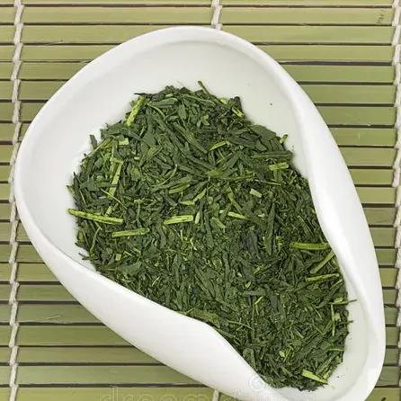 Thé vert en vrac dans un plat blanc sur un fond de bambou.