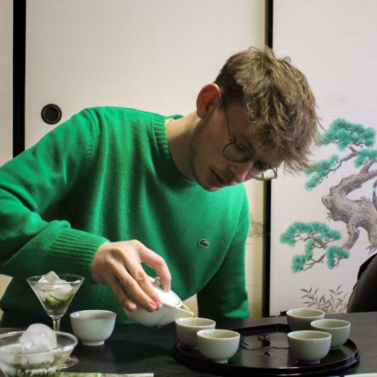 Moi même, pendant ma visite de plantation de thé au Japon Jeune homme avec un pull vert versant du thé dans de petites tasses.